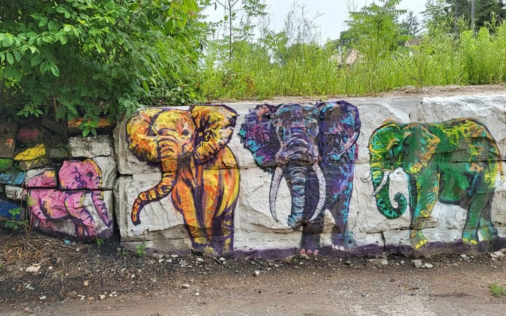 Four colourful elephants painted on a stone retaining wall.